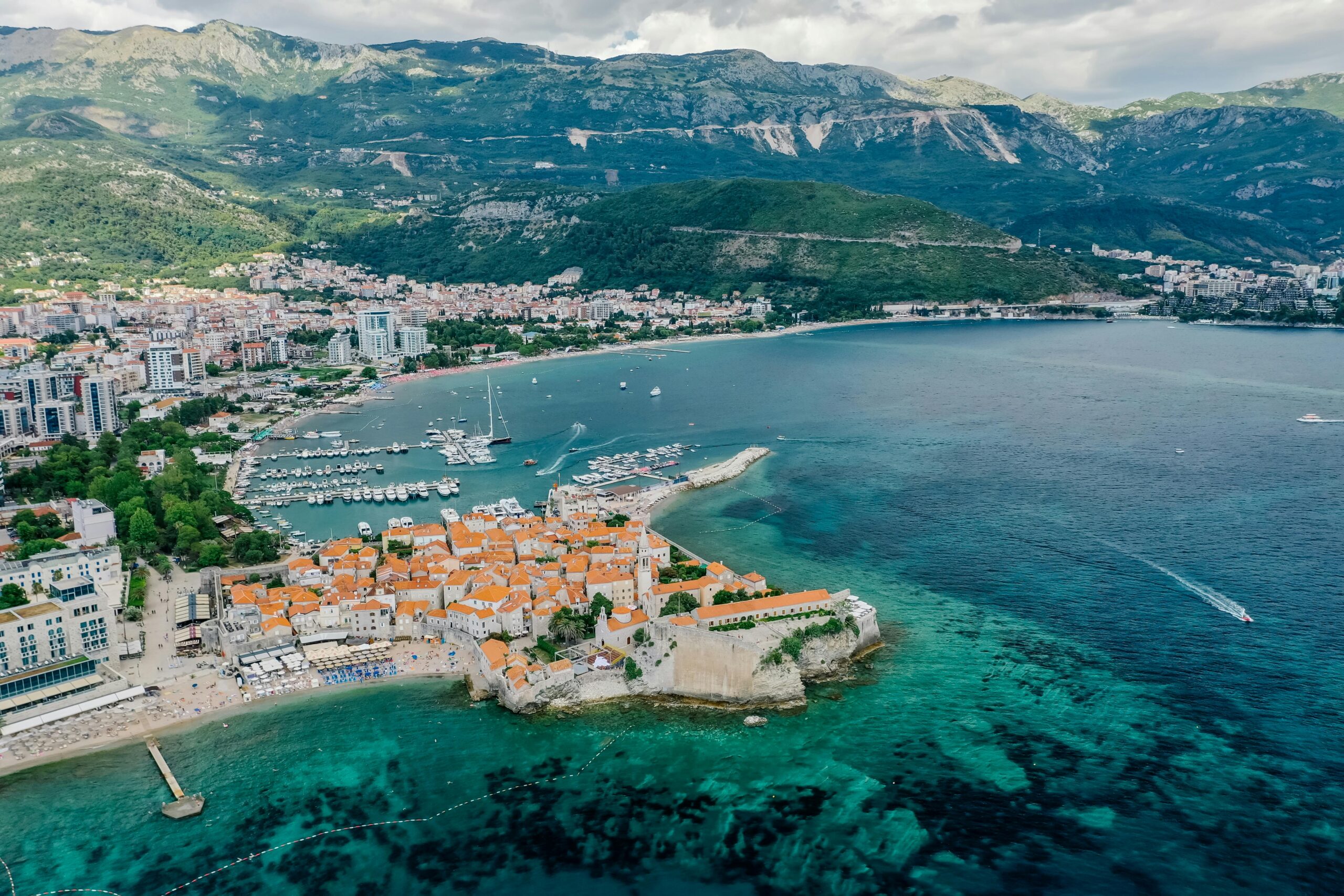 Explore a stunning aerial view of a coastal city with mountains and turquoise waters.