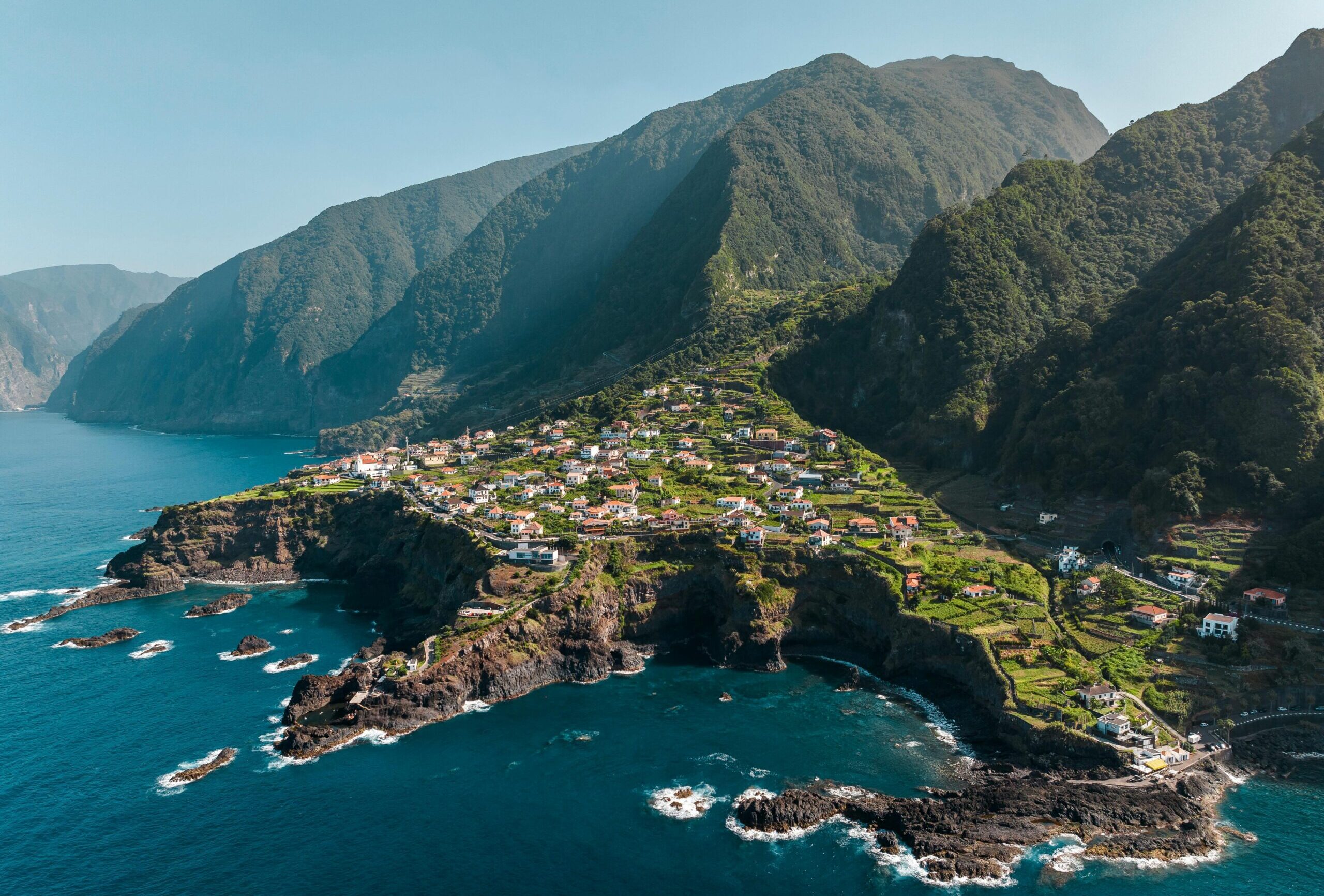 Scenic aerial view of a coastal village in Madeira, Portugal with lush green landscapes and rocky shores.