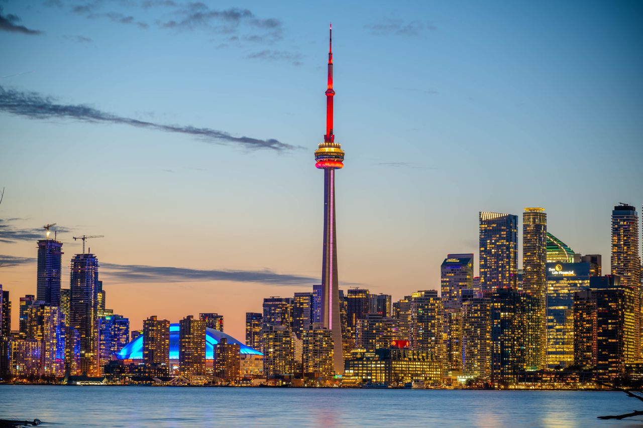 Beautiful sunset view of Toronto skyline with CN Tower and city lights reflecting on the lake.