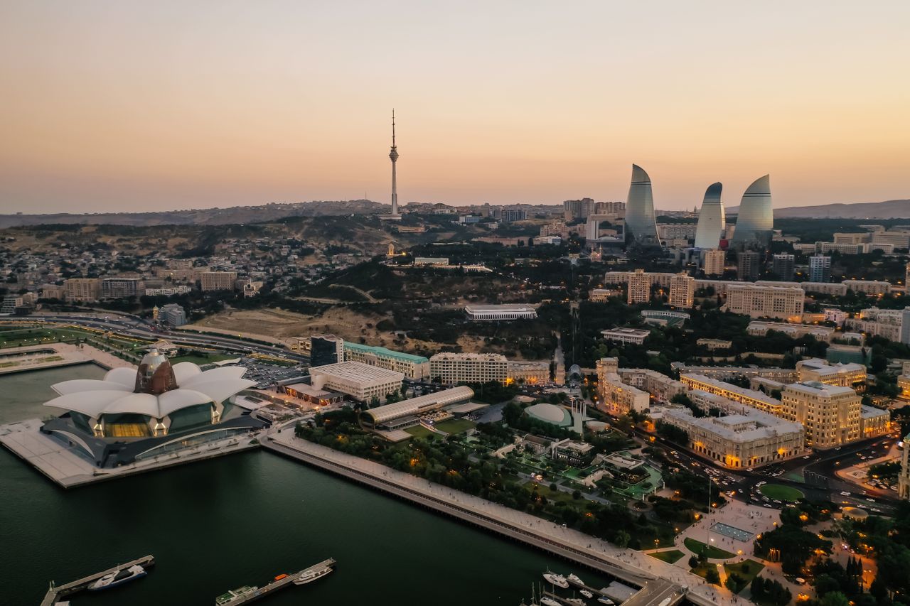 Aerial view of Baku's skyline featuring the Flame Towers and Caspian Sea at dusk.